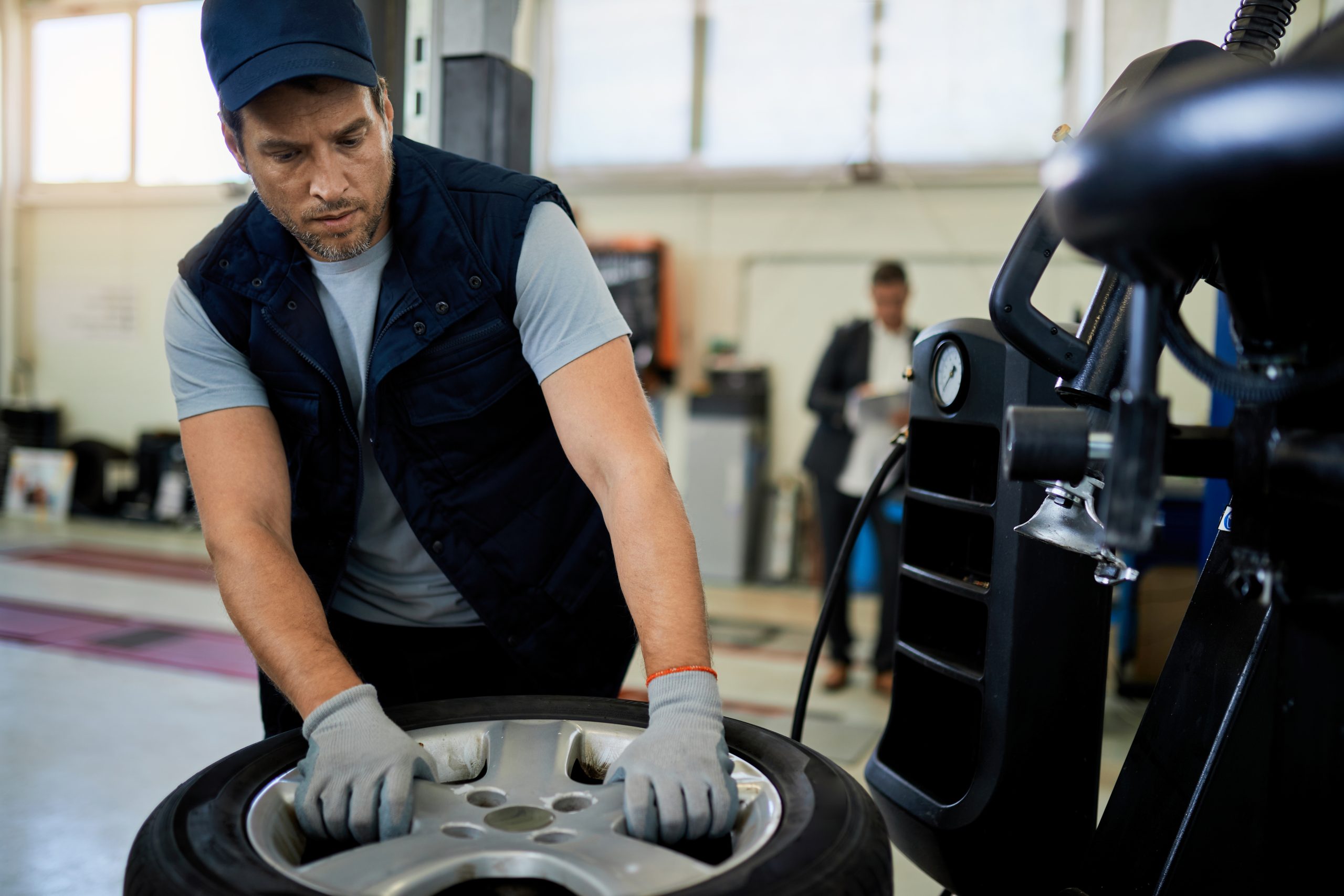 Mid adult mechanic working with car tire in auto repair shop.